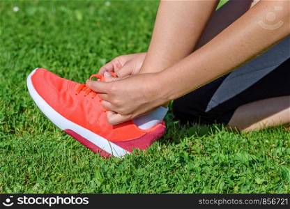 Runner woman kneeling on the grass and tying shoelaces on a sunny day