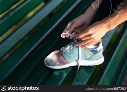 Runner woman tying shoelaces on bench during workout in the park.