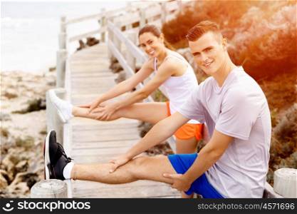 Runners. Young couple exercising and stertching on beach. Runners. Young couple doing sport on beach together