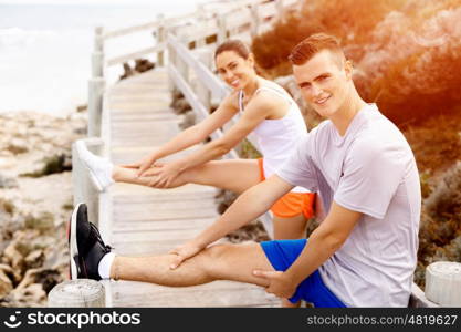 Runners. Young couple exercising and stertching on beach. Runners. Young couple doing sport on beach together