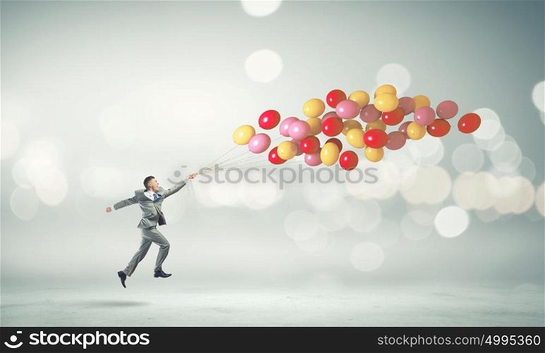 Running businessman. Young cheerful businessman running with bunch of colorful balloons