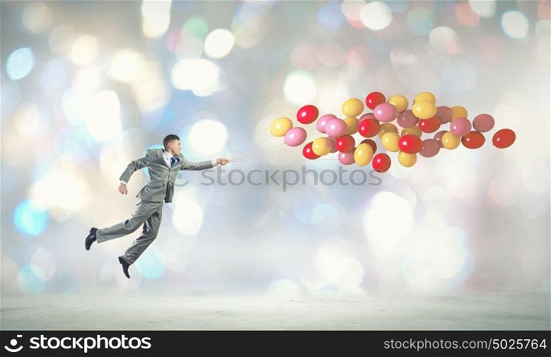 Running businessman. Young cheerful businessman running with bunch of colorful balloons