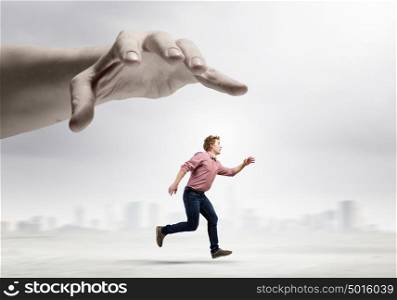 Running from hand. Young man trying to run away from big male hand