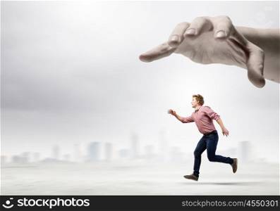 Running man. Young man in casual running away from big hand