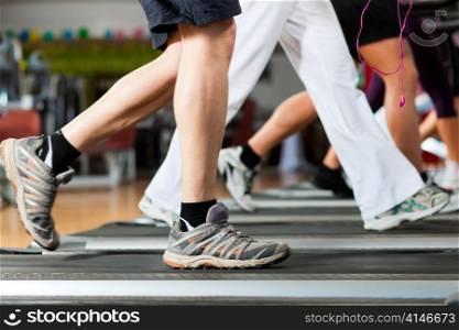 Running on treadmill in gym or fitness club - group of women and men - only legs to be seen - exercising to gain more fitness