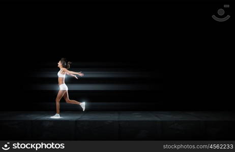 Running woman in sport wear on black background. At full speed