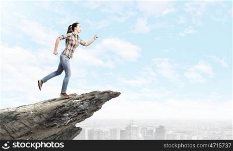 Running woman. Young woman in casual running on edge of rock