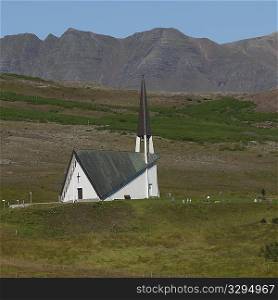 Rural Christian church hidden behind pastureland hillside before mountain