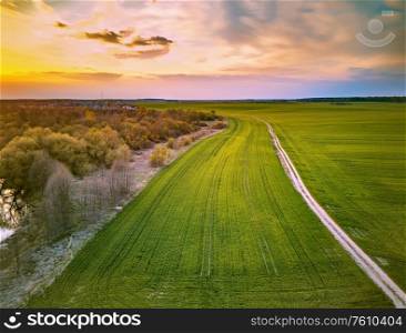 Rural dirt road through spring green fields. Evening countryside scene. April sunset in Belarus aerial view