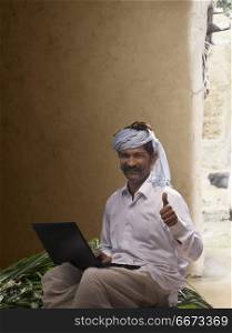Rural farmer showing thumb up while working on laptop