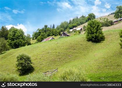 Rural landscape of Carpathian mountains. Small village with traditional wooden houses at sunny day under blue sky
