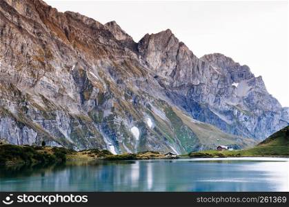 Rural landscape scenery with small cottage on Trubsee lake shore, Swiss alps Mount Graustock peak on background, foot of mount Titlis in Engelberg