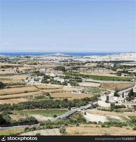 Rural landscape with asphalt roads and fields on Malta. Maltese city on the background of Mediterranean sea.