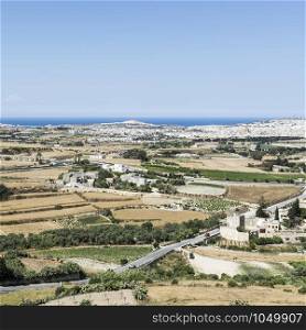 Rural landscape with asphalt roads and fields on Malta. Maltese city on the background of Mediterranean sea.