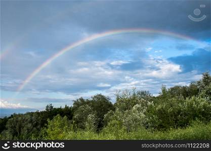 Rural landscape with rainbow over cumulus stormy clouds