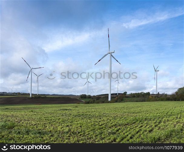 rural landscape with wind turbines and freshly mown grass under blue cloudy sky in german eifel during fall