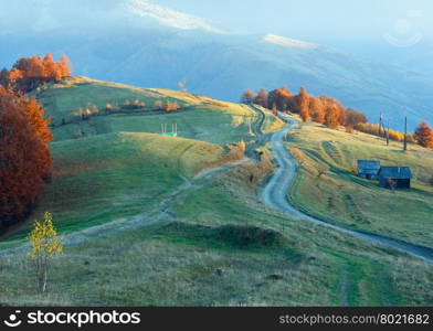 Rural road on autumn mountain misty slope.
