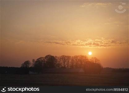 Rural sunset over trees near a farm in a beautiful countryside landscape