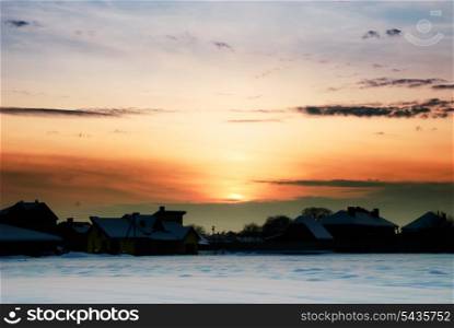 Rural winter landscape with sundown and houses under the snow.