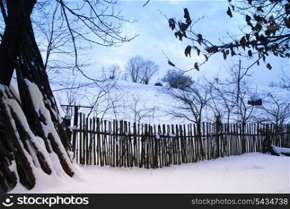 Rural winter mountain landscape with sundown and road, trees, fence