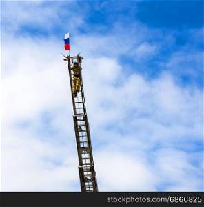 Russia, Kamchatka - April 30, 2017: Celebrating the anniversary of the formation of the fire service in Russia. Fireman on a long fire escape against the blue sky raises the flag