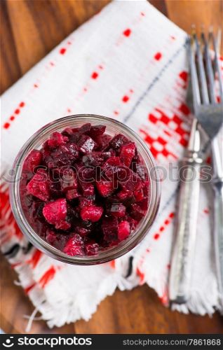 Russian beetroot salad in glass jar over wooden tray, forks, selective focus, top view