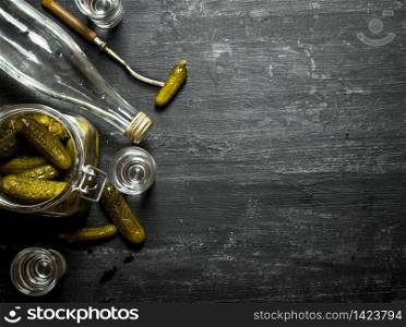 Russian style. Bottle vodka with shot glasses and pickled cucumbers . On a black wooden background.. Russian style. Bottle vodka with shot glasses and pickled cucumbers .