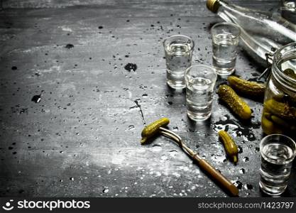 Russian style. Bottle vodka with shot glasses and pickled cucumbers . On a black wooden background.. Russian style. Bottle vodka with shot glasses and pickled cucumbers .