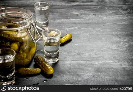 Russian style . Glasses with vodka and pickled gherkins. On a black wooden background.. Russian style . Glasses with vodka and pickled gherkins.