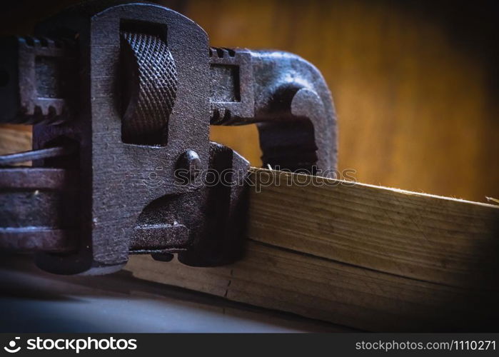 Rusted, stained pipe wrench hand tool clamped with a wooden block