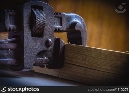 Rusted, stained pipe wrench hand tool clamped with a wooden block