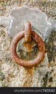 Rusted steel mooring ring attached to cement on rock wall.