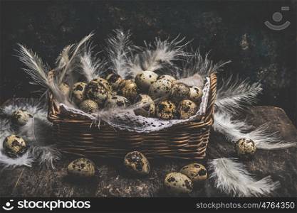 Rustic Basket with quail eggs and feathers on dark wooden background