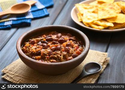 Rustic bowl of chili con carne with homemade tortilla chips in the back, photographed with natural light (Selective Focus, Focus one third into the chili)