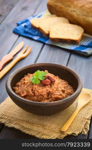 Rustic bowl of homemade red kidney bean spread garnished with kidney beans and fresh coriander leaf, wholegrain bread in the back, photographed with natural light (Selective Focus, Focus on the leaf)