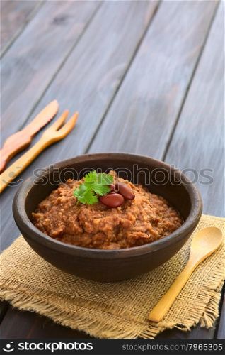 Rustic bowl of homemade red kidney bean spread garnished with kidney beans and fresh coriander leaf, photographed on dark wood with natural light (Selective Focus, Focus on the leaf)