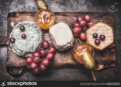 Rustic cheese plate with various cheese, grape and honey mustard sauces, top view. Dark style