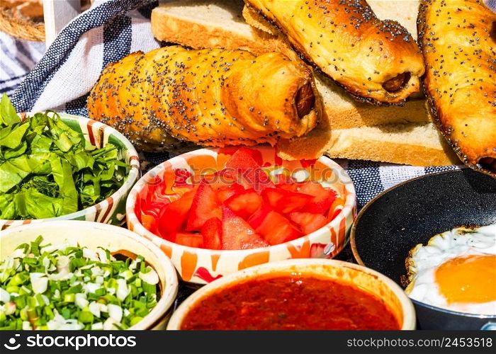 Rustic composition with sausages rolls and different bowls with sauce and chopped vegetables ( tomatoes, green lettuce, green onion, green garlic)