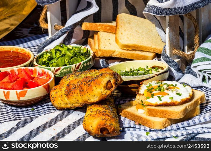 Rustic composition with sausages rolls, fried egg on toast bread, different bowls with sauce and chopped vegetables.