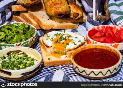 Rustic composition with sausages rolls, fried egg on toast bread, different bowls with sauce and chopped vegetables.