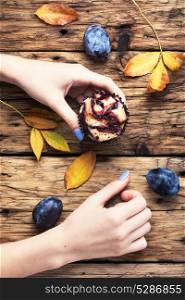 rustic cupcake with plum. Hand with cupcake above the table with autumn leaves