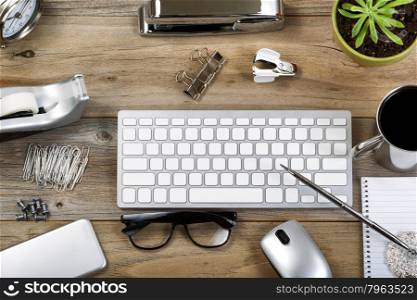 Rustic desktop with work accessories. Objects in and out of frame layout with mostly silver color items.