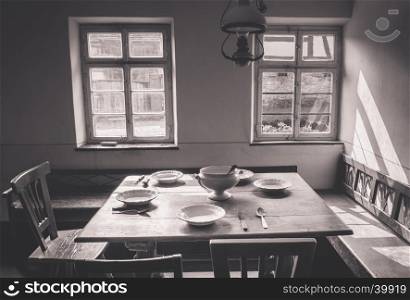 Rustic dining room in vintage settings with wooden table, chairs and benches. Old dishes and tableware are placed on the table.