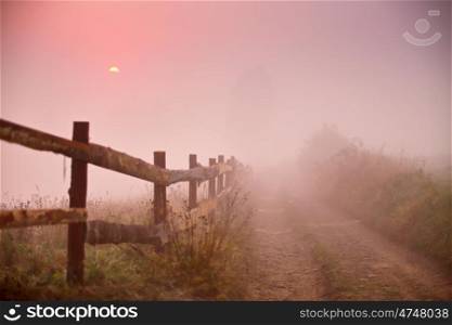 Rustic fence. Fence and dirt road at foggy morning. Misty rural scene