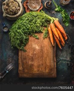 Rustic food background with bunch of carrots with greens on cutting board. Top view. Frame. Healthy home cooking. Homemade cuisine