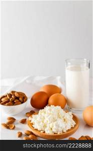 Rustic homemade protein balanced diet food. Cottage cheese, eggs, nuts and milk on a white background. Vertical photo. Protein food on a white background - cottage cheese, eggs, nuts. A set of healthy foods for a balanced diet.