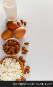 Rustic homemade protein balanced diet food. Cottage cheese, eggs, nuts and milk on a white background. Vertical photo. Protein food on a white background - cottage cheese, eggs, nuts. A set of healthy foods for a balanced diet.