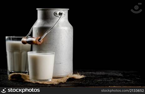 Rustic milk in a can and a glass on the table. On a black background. High quality photo. Rustic milk in a can and a glass on the table.