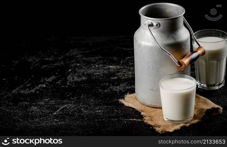 Rustic milk in a can and a glass on the table. On a black background. High quality photo. Rustic milk in a can and a glass on the table.