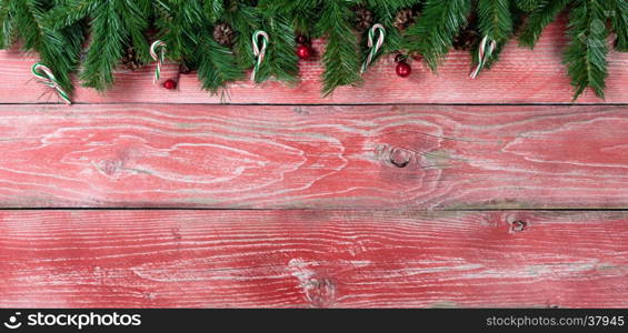 Rustic red wooden background for Christmas concept with fir branches, candy canes, red berries and pine cones. Overhead view with copy space